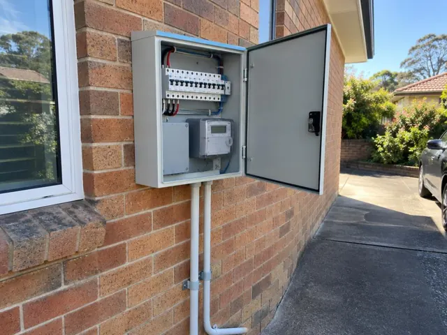 Open electrical switchboard on a brick exterior wall beside a driveway in Beacon Hill
